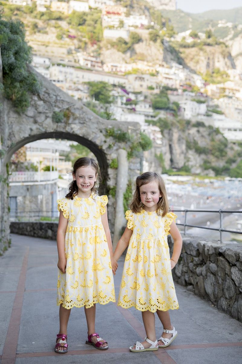 Two young sisters in matching yellow eyelet dresses on a Positano street