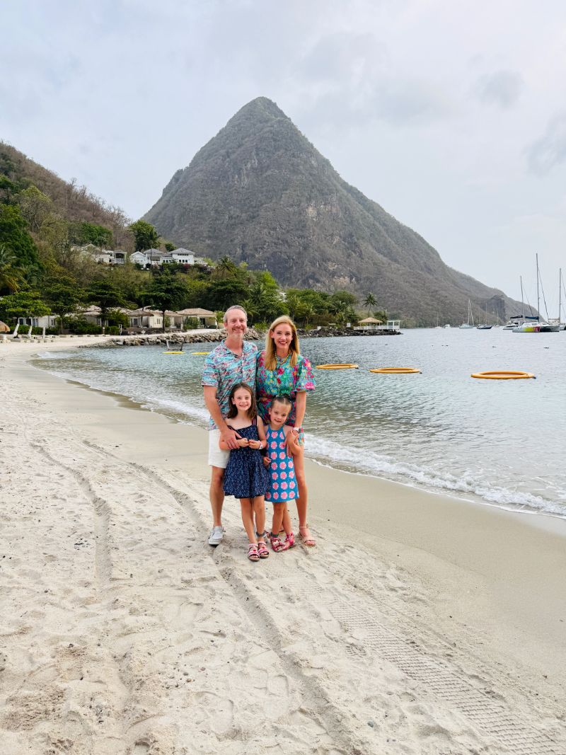Family walking on the wide white sand of Sugar Beach in St. Lucia with a single Piton rising dramatically in the background