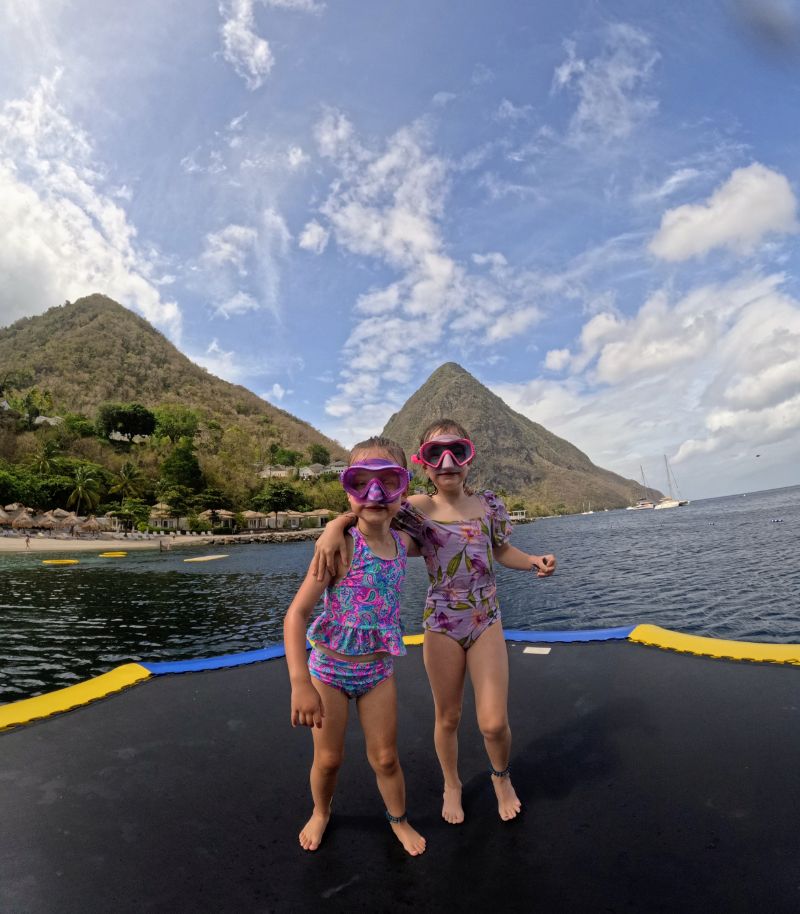 Two girls in snorkel gear standing on Sugar Beach with both St. Lucia Pitons visible behind them